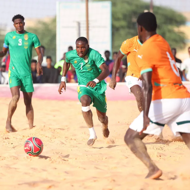 Un joueur mauritanien en vert conduit le ballon face à des joueurs ivoiriens sur le sable