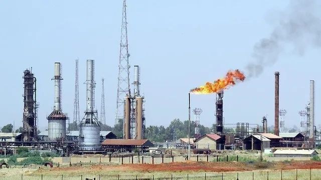 Une installation pétrolière avec tours, réservoirs et une torchère allumée sous un ciel clair, image d'illustration d'archives