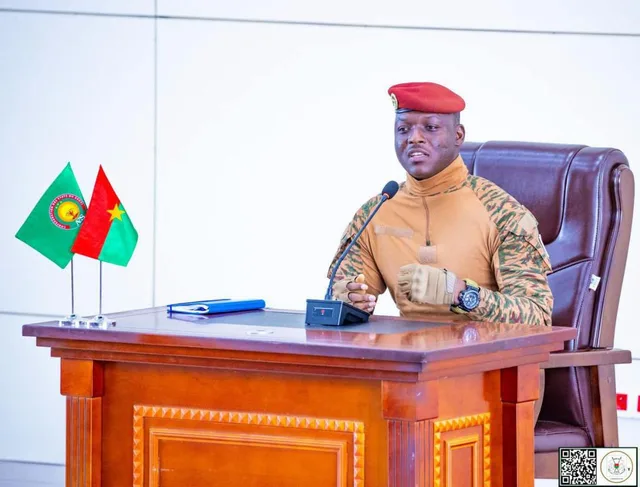 Ibrahim Traoré en tenue militaire et béret rouge, parlant derrière un bureau devant un micro, à côté des drapeaux du Burkina et de l'AES, photo d'archives