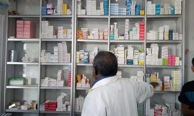 Un pharmacien en blouse blanche, de dos, prend une boîte sur des rayons remplis de médicaments, photo d'illustration d'archives
