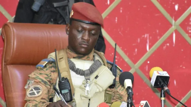 Le capitaine Ibrahim Traoré en treillis et béret rouge signant un document devant des micros