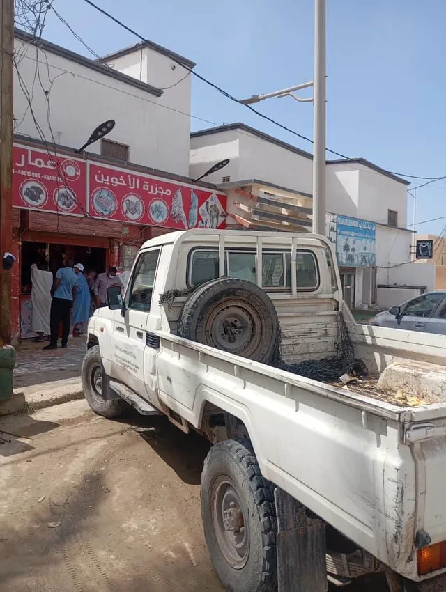 Un pick-up blanc garé devant une boucherie à l'enseigne rouge à Nouakchott
