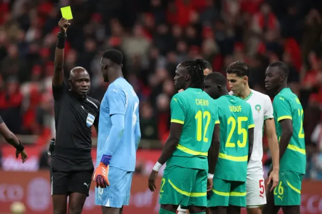 Un arbitre brandit un carton jaune devant des joueurs du Sénégal et du Maroc
