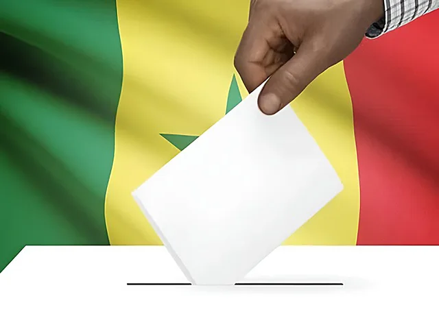 Une main glisse un bulletin dans une urne devant le drapeau sénégalais