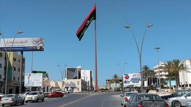 Un grand mât portant le drapeau libyen au centre d'un rond-point entouré de voitures, d'immeubles et de panneaux, photo d'archives
