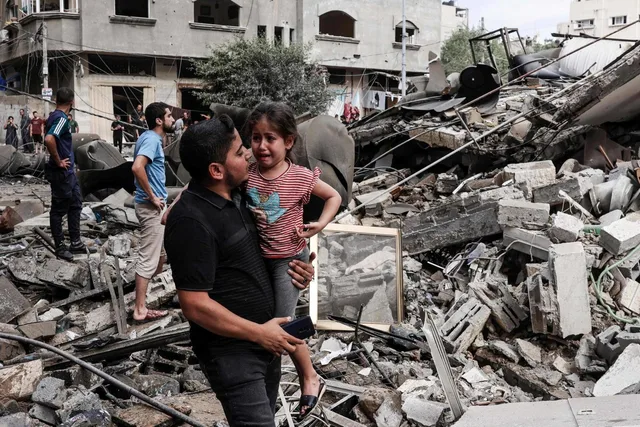 Un homme porte une fillette en pleurs au milieu des décombres de bâtiments détruits dans la bande de Gaza, photo d'archives