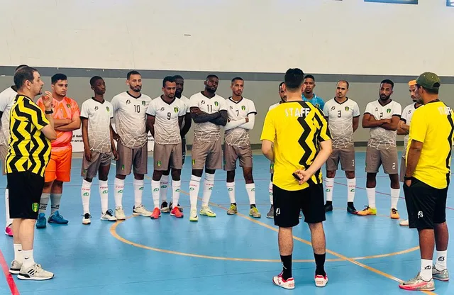 Des joueurs de futsal en maillot blanc écoutent leur entraîneur dans une salle de sport