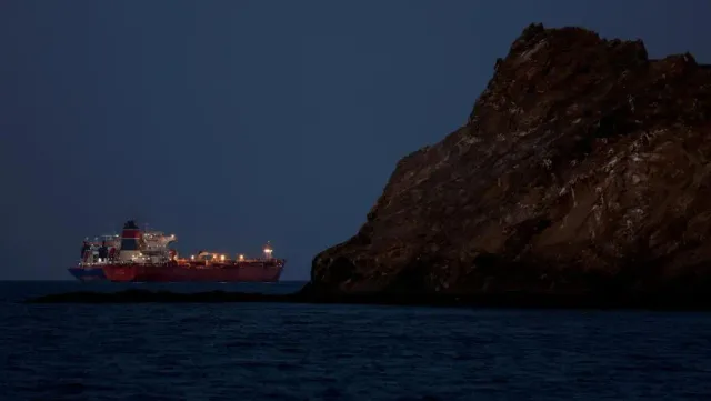 Un pétrolier rouge éclairé naviguant près d'une falaise rocheuse au crépuscule, photo d'archives