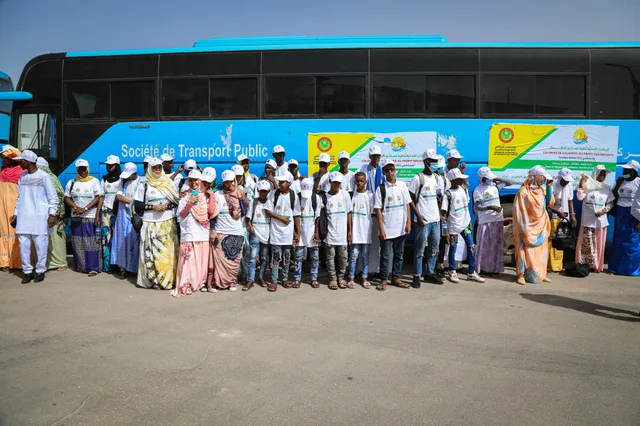 Un groupe d'enfants en t-shirts et casquettes blancs devant un bus de transport public à Nouakchott