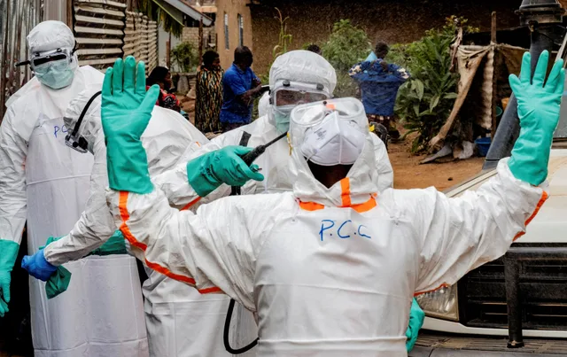 Des soignants en combinaison de protection blanche et gants verts se font désinfecter lors d'une opération de riposte contre Ebola