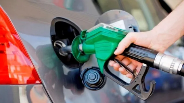 Main tenant un pistolet de pompe à carburant vert dans le réservoir d'une voiture grise, photo d'archives