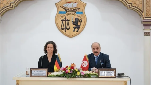 L'emblème de la République tunisienne accroché à un mur blanc derrière une table officielle portant les drapeaux tunisien et allemand, photo d'archives
