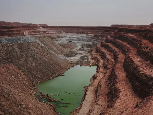 Une vaste mine à ciel ouvert aux gradins de terre rouge, avec une mare verte au fond, en plein désert, photo d'archives