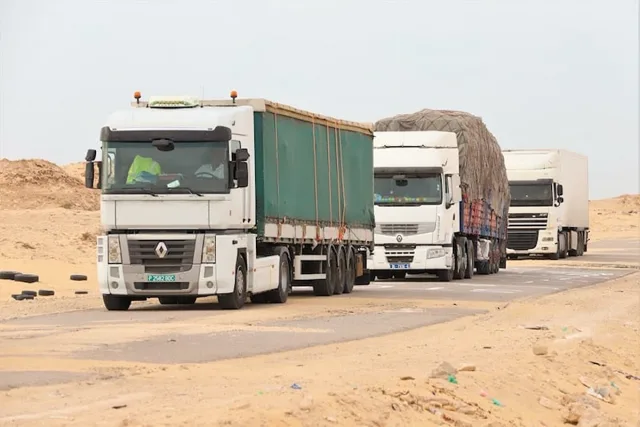 Trois camions de marchandises circulent sur une route bordée de sable, photo d'archives