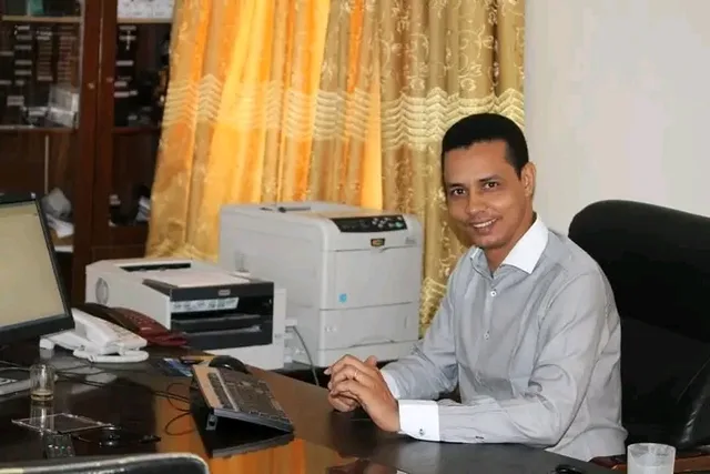 Un homme souriant assis à un bureau avec un ordinateur et une imprimante