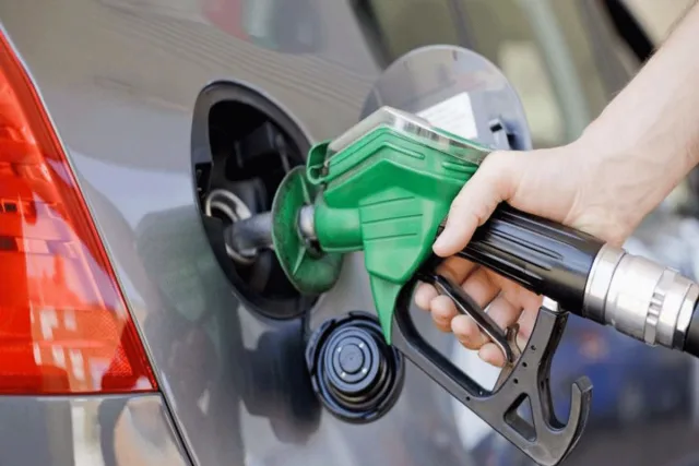 Une main tenant un pistolet de pompe à carburant vert dans le réservoir d'une voiture, photo d'archives