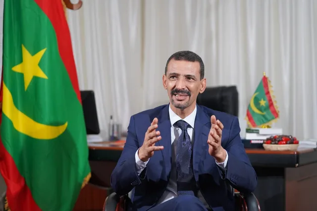 El Houssein Ould Meddou s'exprimant dans son bureau, devant le drapeau mauritanien