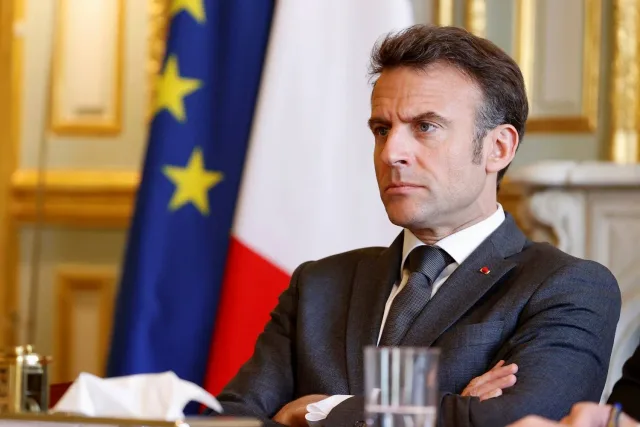Le président français Emmanuel Macron assis devant les drapeaux français et européen