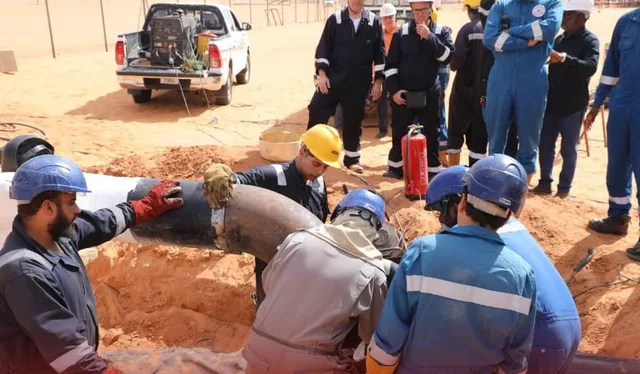 Des ouvriers casqués en combinaison fixant un tuyau dans une tranchée en terrain désertique, photo d'archives