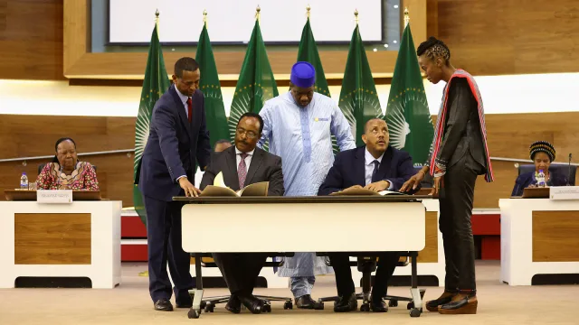 Deux représentants assis signent des documents derrière une table blanche, entourés de médiateurs devant des drapeaux verts de l'Union africaine, photo d'archives