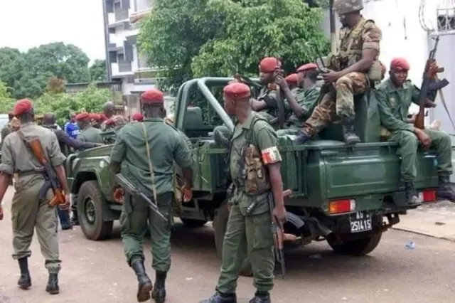 Militaires guinéens en béret rouge, armés, autour d'un véhicule militaire vert dans une rue, photo d'archives