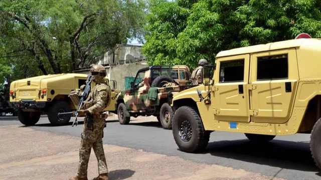 Un soldat malien armé debout près de véhicules militaires dans une rue