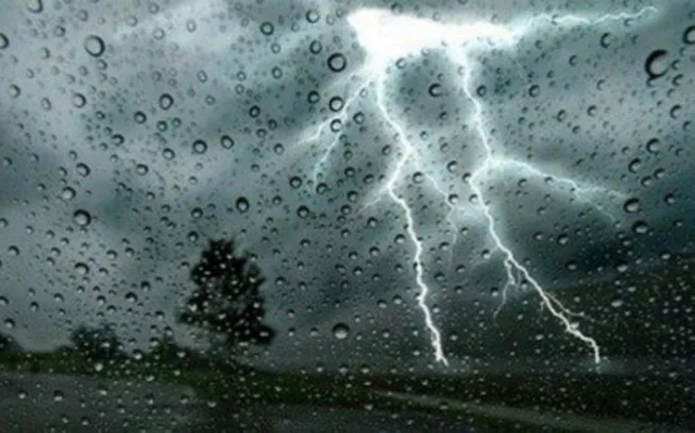 Éclair dans un ciel chargé derrière une vitre couverte de gouttes de pluie, image d'illustration
