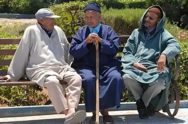 Trois hommes âgés en djellaba assis sur un banc dans un jardin, photo d'archives