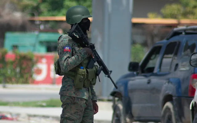 Un membre des forces de sécurité masqué, en treillis et casque, tenant un fusil, l'écusson haïtien à l'épaule, près d'un 4x4, photo d'archives