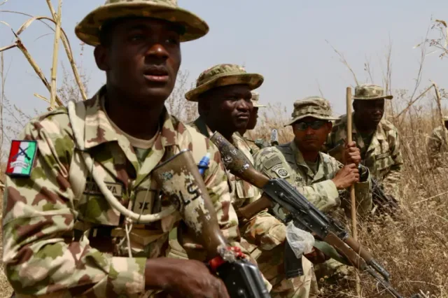 Soldats nigérians en treillis et chapeaux de brousse, armes à la main, dans des herbes sèches lors d'un exercice, photo d'archives