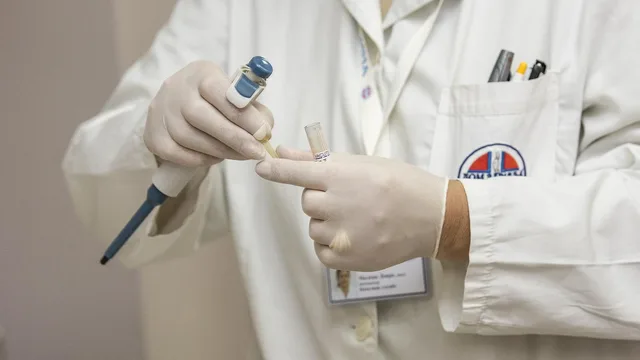 Mains gantées tenant une pipette et un tube d'échantillon devant une blouse blanche, image d'illustration