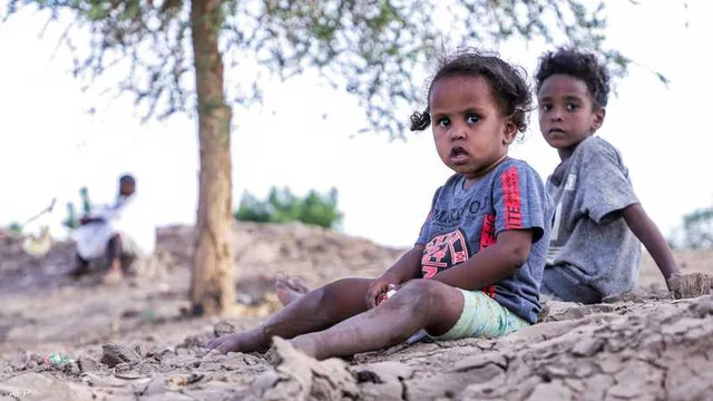 Deux jeunes enfants soudanais assis sur une terre sèche et craquelée sous un arbre, un homme assis en arrière-plan, photo d'archives