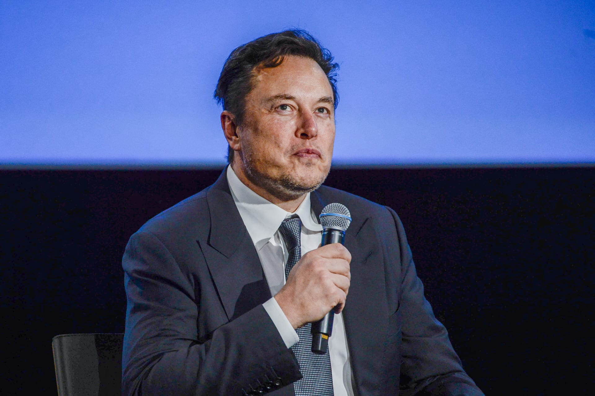 Elon Musk s’exprimant au micro devant un fond bleu