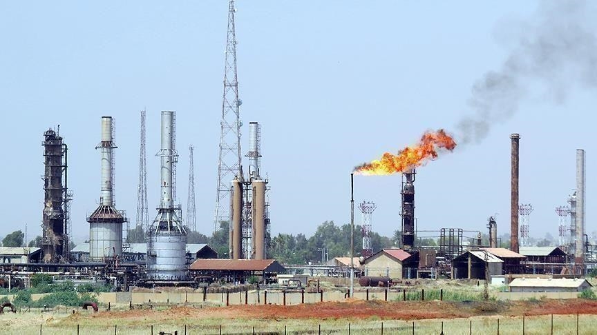 Une installation pétrolière avec tours, réservoirs et une torchère allumée sous un ciel clair, image d'illustration d'archives