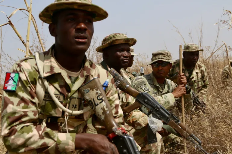 Soldats nigérians en treillis et chapeaux de brousse, armes à la main, dans des herbes sèches lors d'un exercice, photo d'archives