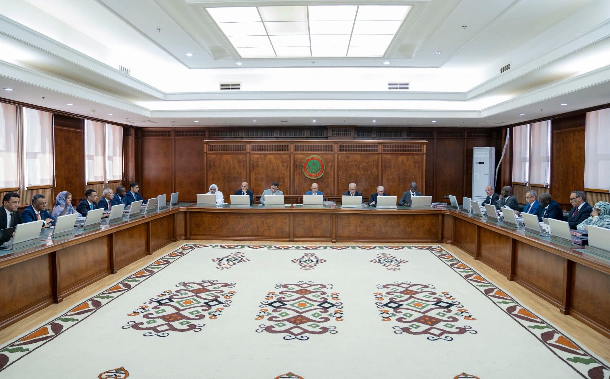 Une grande salle de réunion officielle où des membres du gouvernement sont assis autour de tables en bois