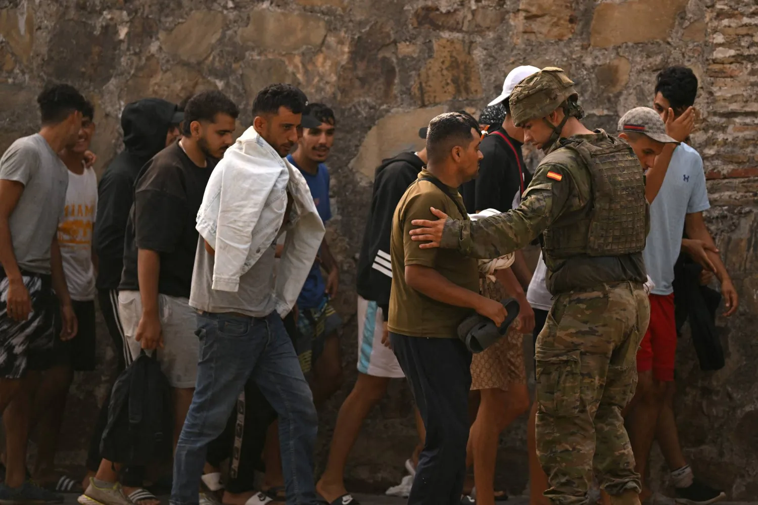 Un soldat espagnol encadre un groupe de jeunes migrants près d'un mur de pierre à Ceuta