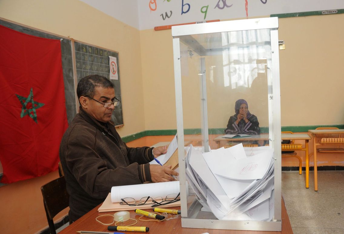 Un agent assis près d'une urne transparente remplie de bulletins dans une salle de classe transformée en bureau de vote au Maroc, photo d'archives