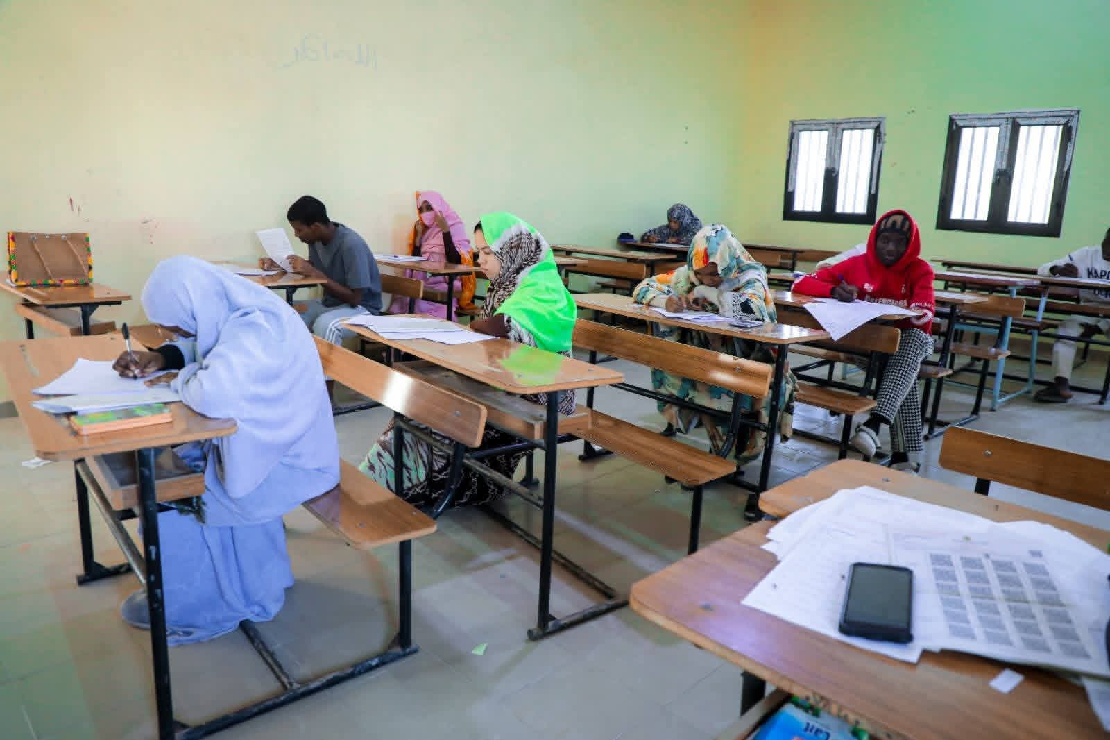 Des élèves assis à des tables dans une salle d'examen, écrivant sur des copies