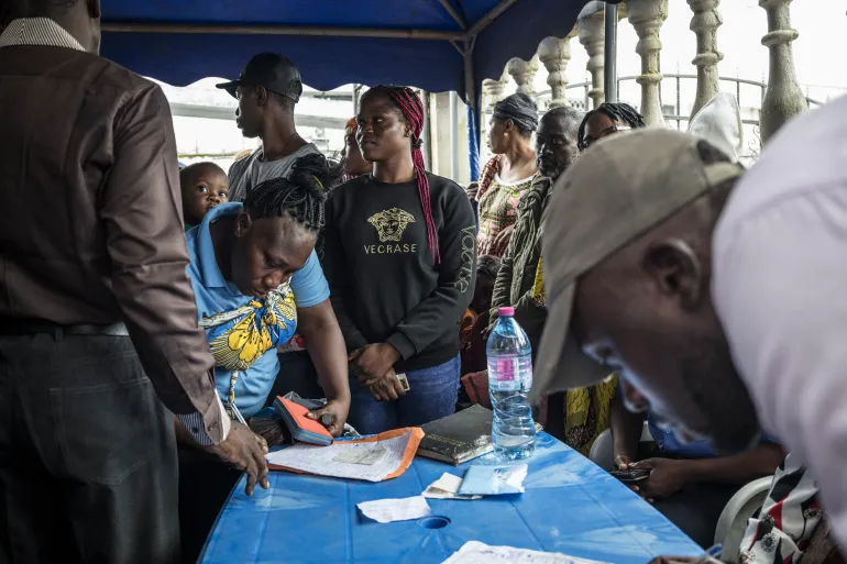 Des électeurs font la queue devant une table sous une tente bleue tandis que des agents consignent des informations dans un bureau de vote au Cameroun