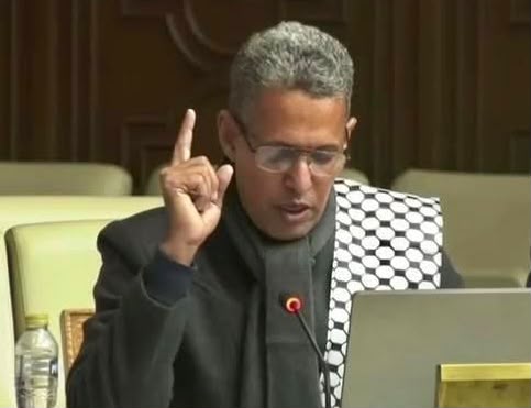 Un député portant des lunettes s'exprime au micro dans un hémicycle