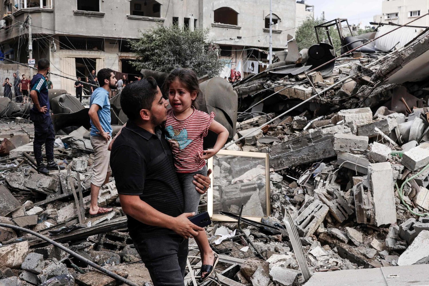 Un homme porte une fillette en pleurs au milieu des décombres de bâtiments détruits dans la bande de Gaza, photo d'archives