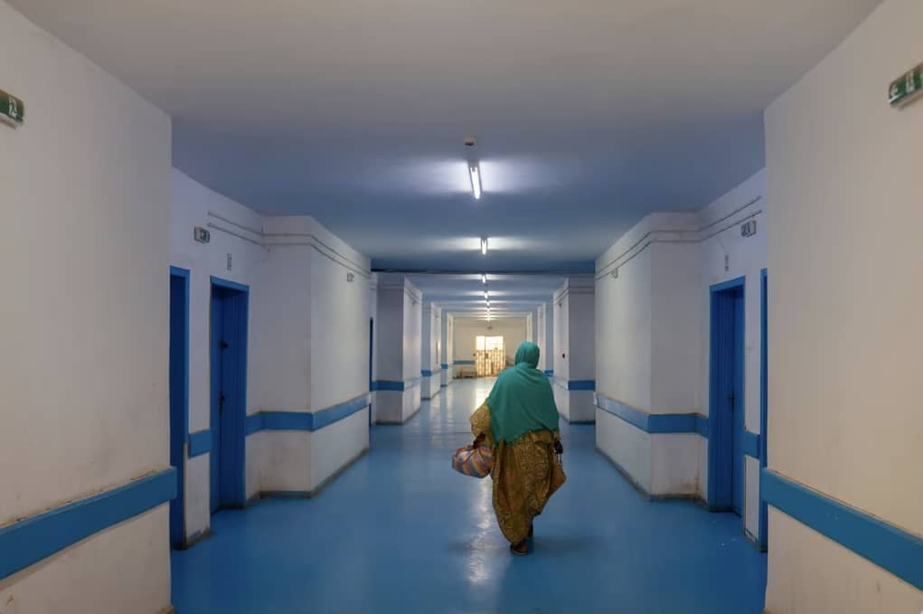 Un long couloir d'hôpital aux portes bleues où une femme marche de dos, image d'illustration d'archives