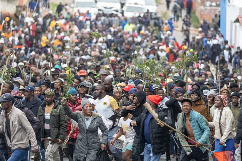 Une foule de manifestants, certains munis de bâtons et de branches, défile dans une rue d'Afrique du Sud lors d'une marche contre les immigrés