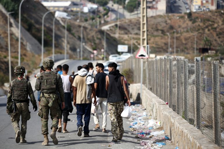 Deux soldats espagnols marchant derrière un groupe de jeunes hommes sur une route longeant une clôture frontalière à Ceuta, photo d'archives