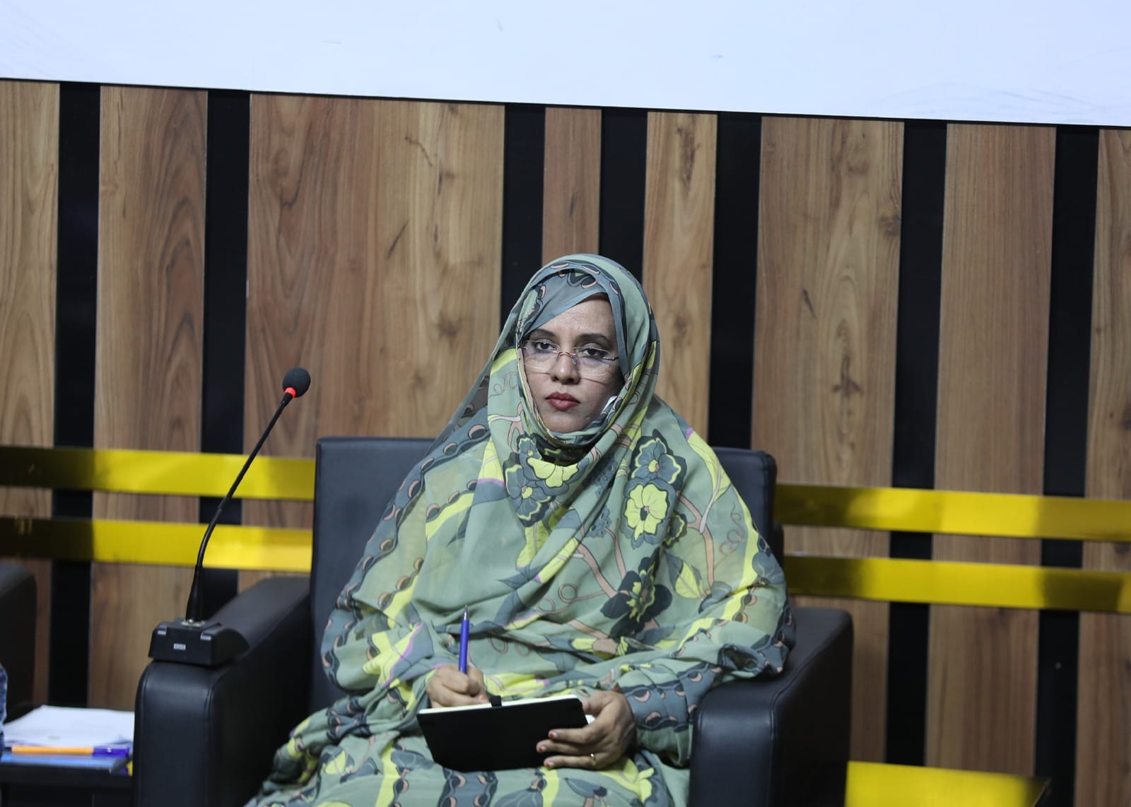 La ministre mauritanienne de l'Éducation assise sur une estrade, un stylo et un carnet à la main