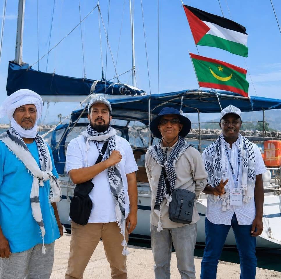Quatre hommes portant le keffieh devant un voilier arborant les drapeaux palestinien et mauritanien, photo d'archives de participants à la flottille Sumud