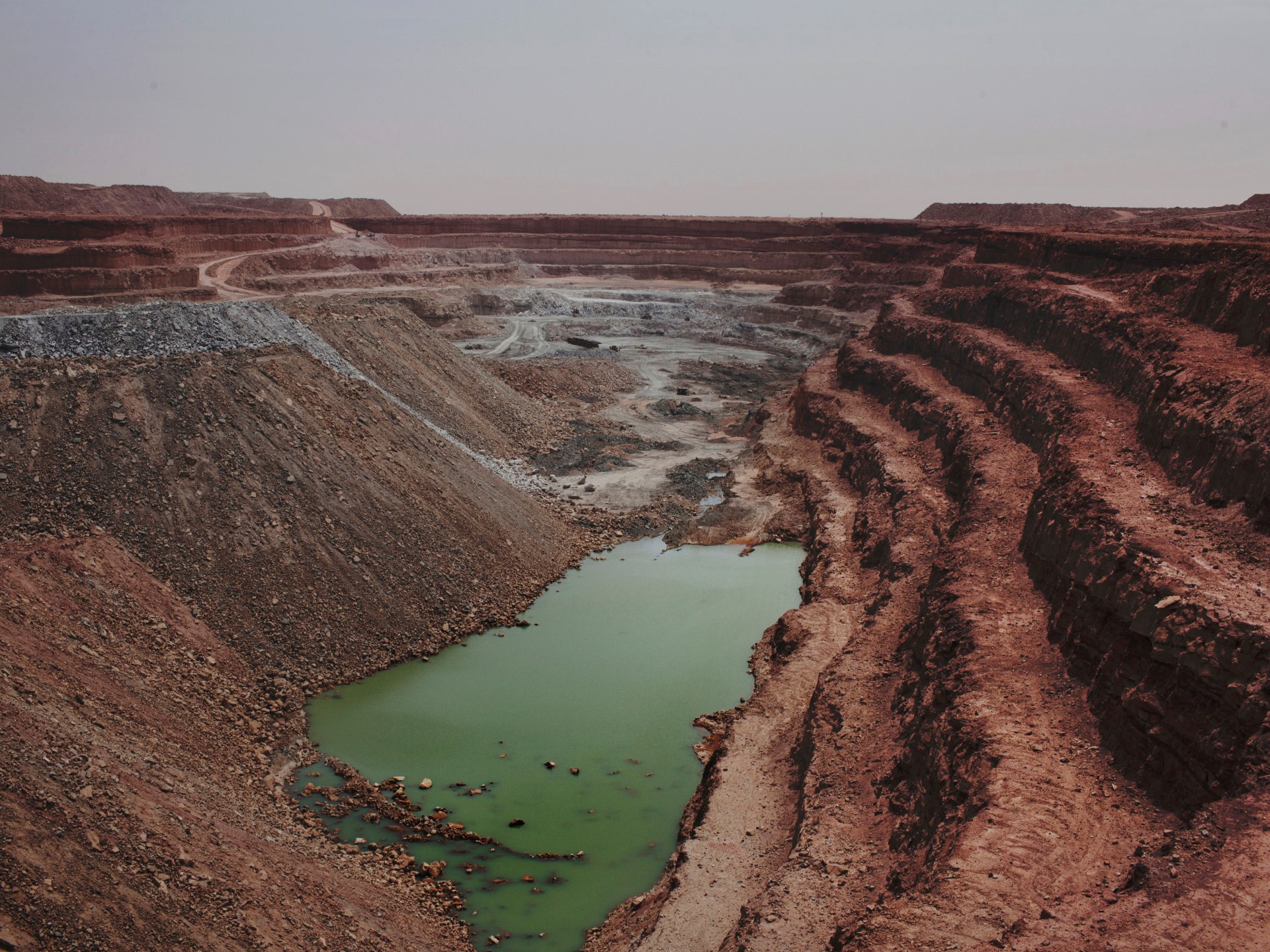 Une vaste mine à ciel ouvert aux gradins de terre rouge, avec une mare verte au fond, en plein désert, photo d'archives