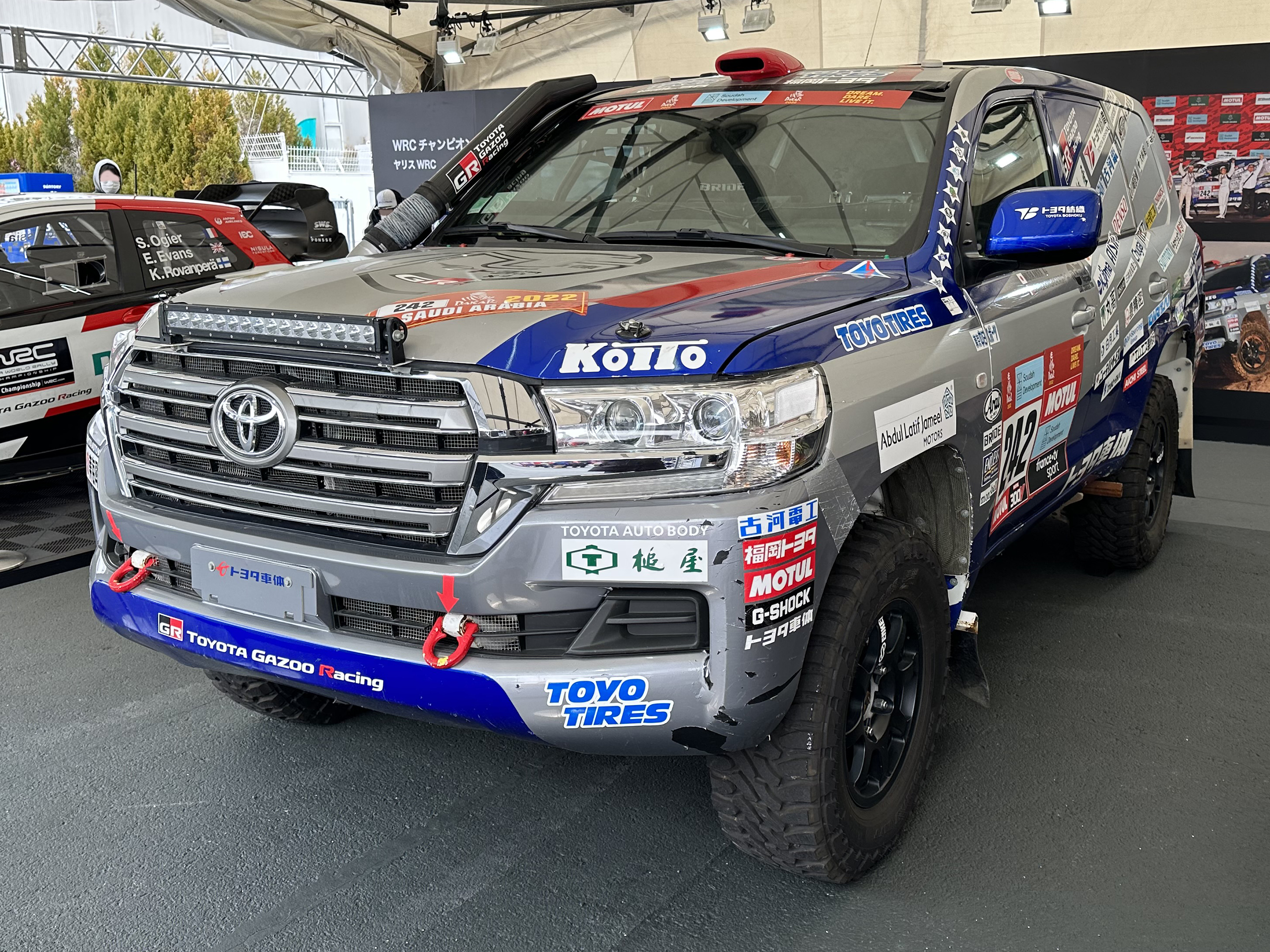 Une voiture de rallye aux couleurs du Dakar 2022 exposée sous un stand