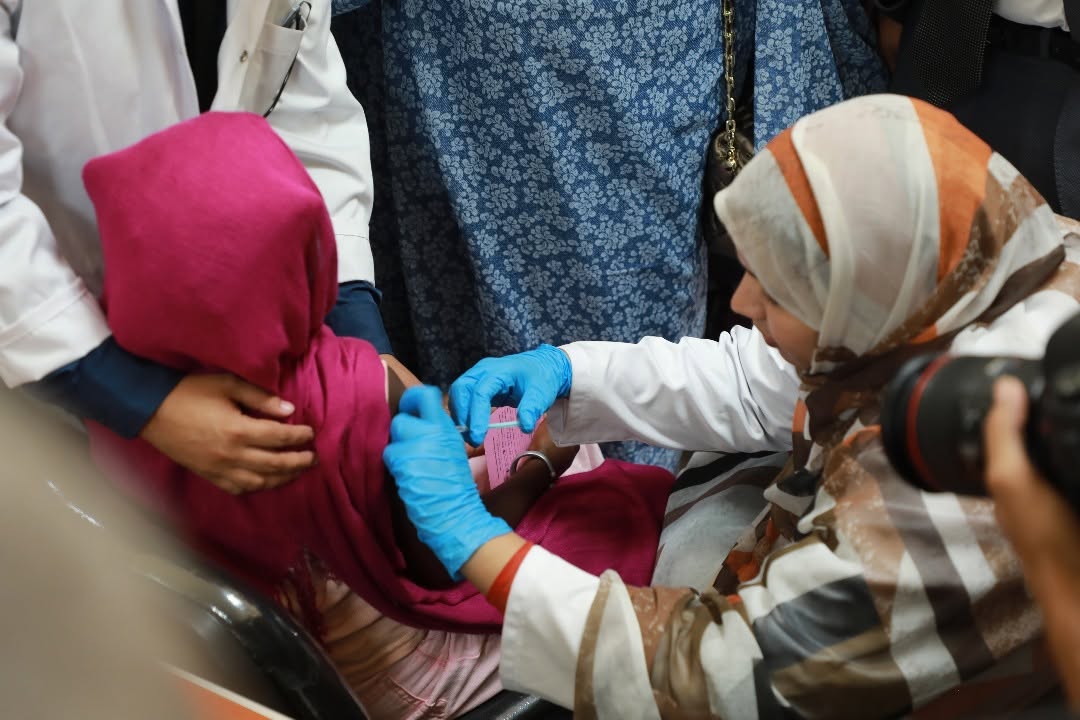 Une agente de santé gantée de bleu vaccine au bras une fillette dont le visage est couvert d'un foulard, photo d'archives
